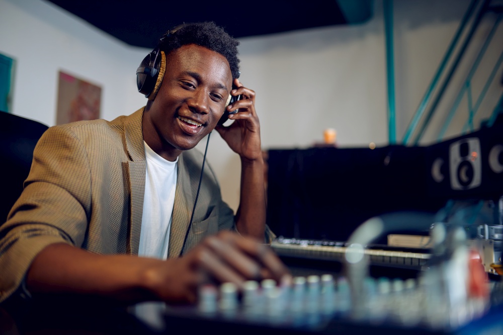 Happy male dj in headphones, recording studio interior on background. Synthesizer and audio mixer, musician workplace, creative process. Happy male dj in headphones, recording studio