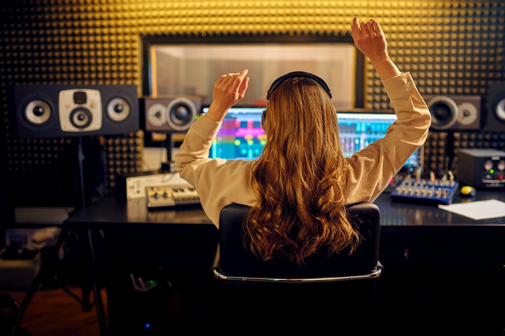 Female sound engineer at mixing consol, back view, recording studio interior on background. Synthesizer and audio mixer, musician workplace, creative process. Female sound engineer at mixing consol, back view