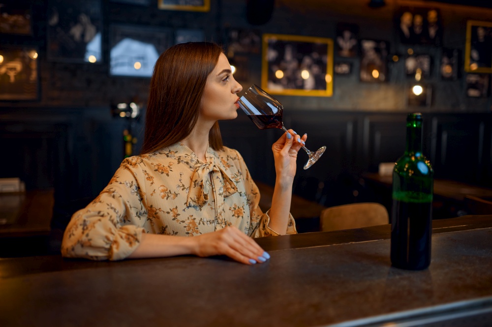 Young woman drinks red wine at the counter in bar. One female person in pub, human emotions, leisure activities, nightlife. Young woman drinks red wine at the counter in bar