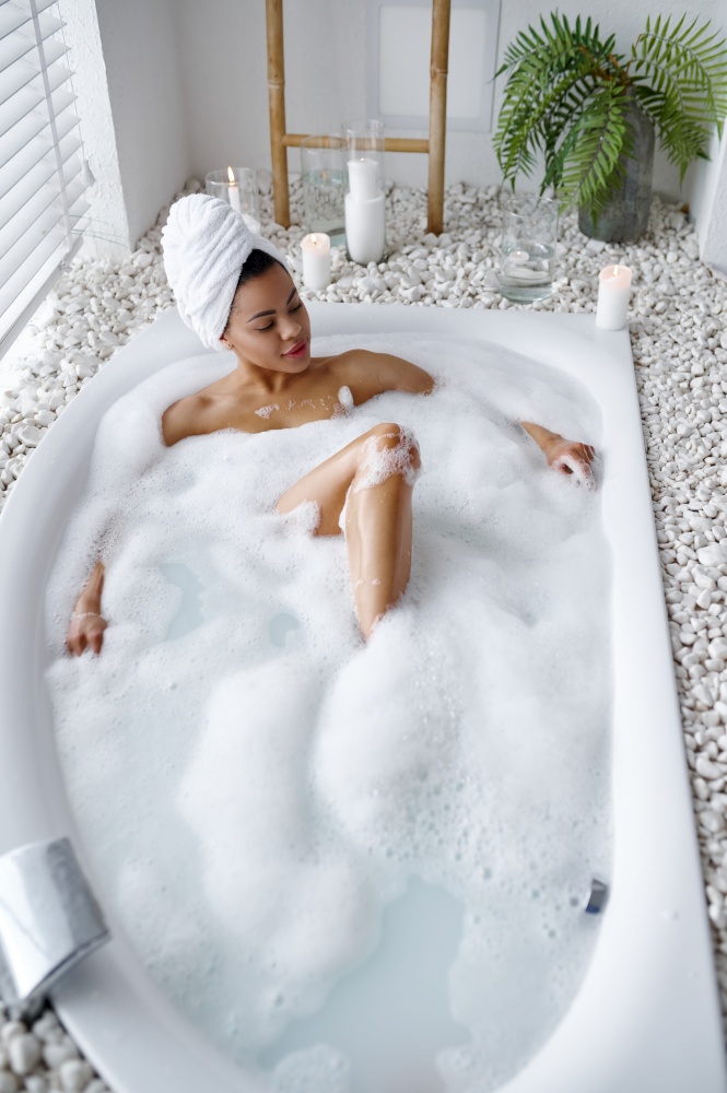 Attractive woman relax in the bath with foam. Female person in bathtub, beauty and health care in spa, wellness treathment in bathroom, pebbles and candles on background. Attractive woman relax in the bath with foam