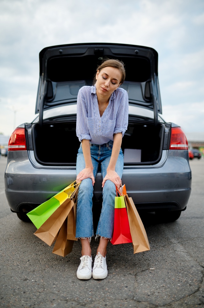 Woman with bags at the opened trunk on supermarket car parking. Happy customer carrying purchases from the shopping center, female buyer with packages. Woman with bags at the opened trunk on parking