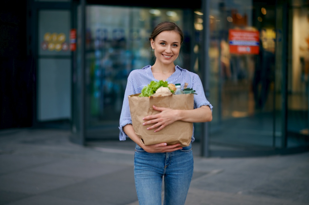 Woman with food in cardboard bag on supermarket car parking. Happy customer with purchases near the shopping center, female person buying fruits and vegetables. Woman with food in bag on supermarket car parking