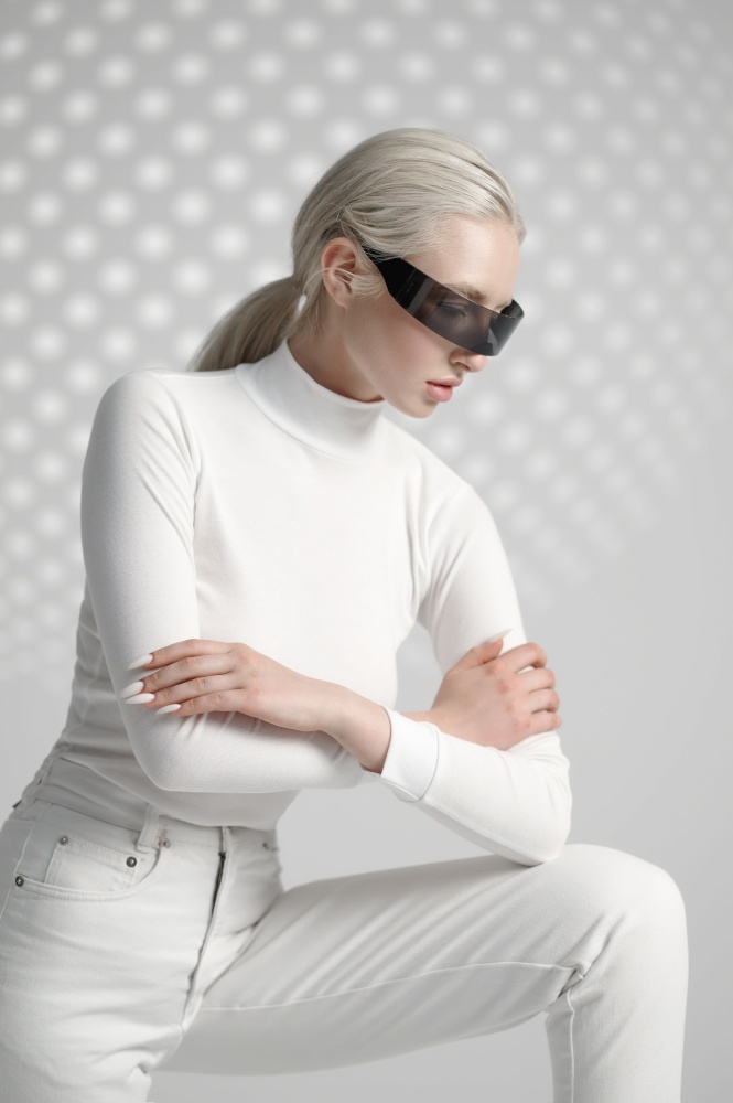Model in white clothes and futuristic glasses, light grey background. Female person in virtual reality style, future technology, futurism concept. Model in white clothes and futuristic glasses