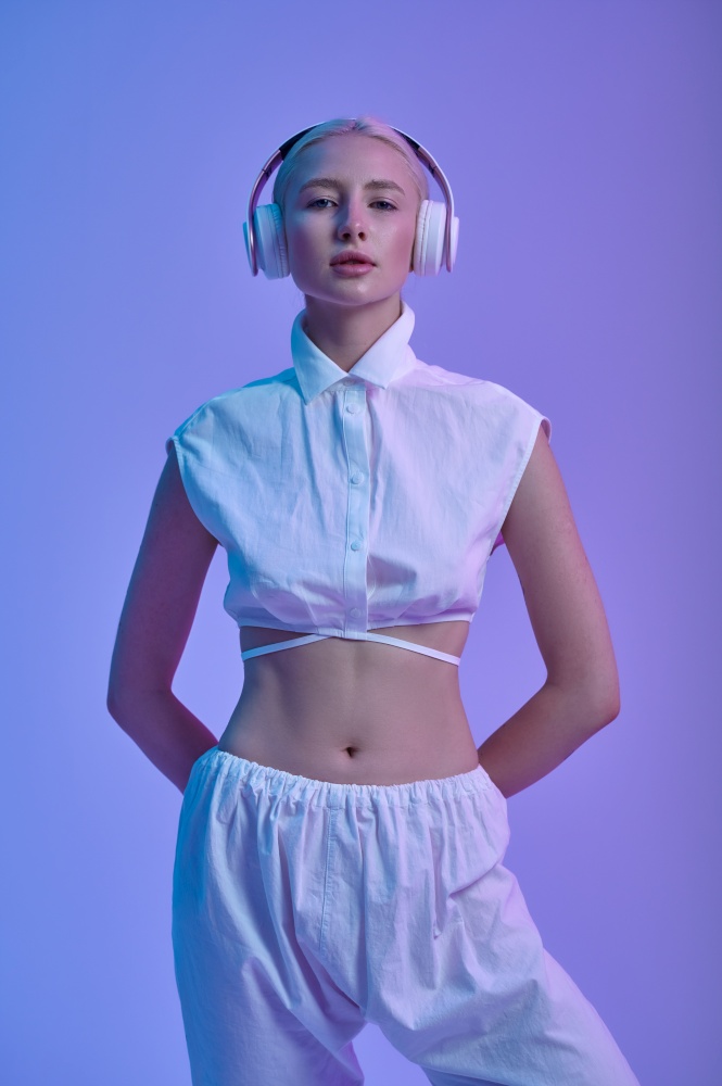 Attractive futuristic woman in white clothes and modern headphones, blue background. Sexy female person in virtual reality style, future technology, futurism concept. Attractive futuristic woman in modern headphones