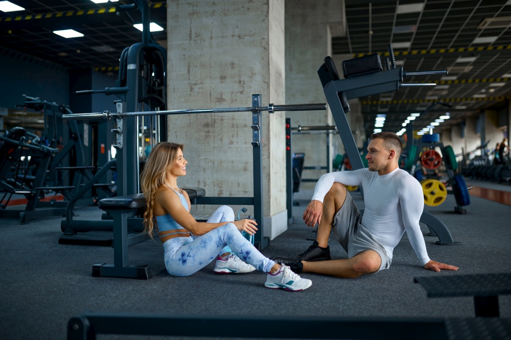 Couple relax on the floor after fitness training in gym. Athletic man and woman on workout in sport club, active healthy lifestyle. Couple relax after fitness training in gym
