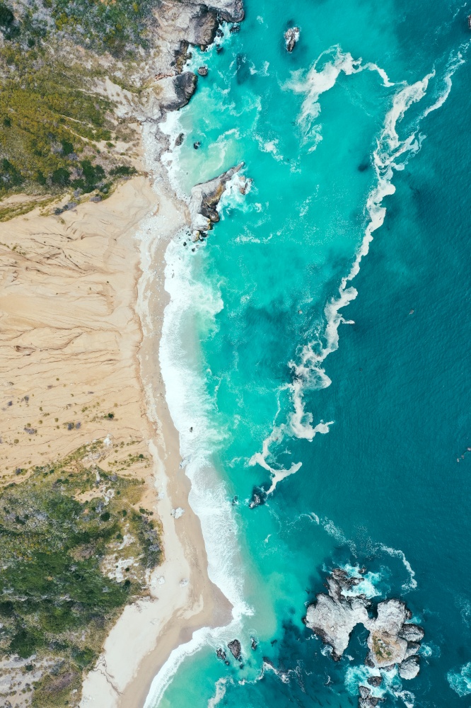 A vertical overhead shot of the beautiful shoreline of the sea with blue clean water and sandy beach. Vertical overhead shot of the beautiful shoreline of the sea with blue clean water and sandy beach