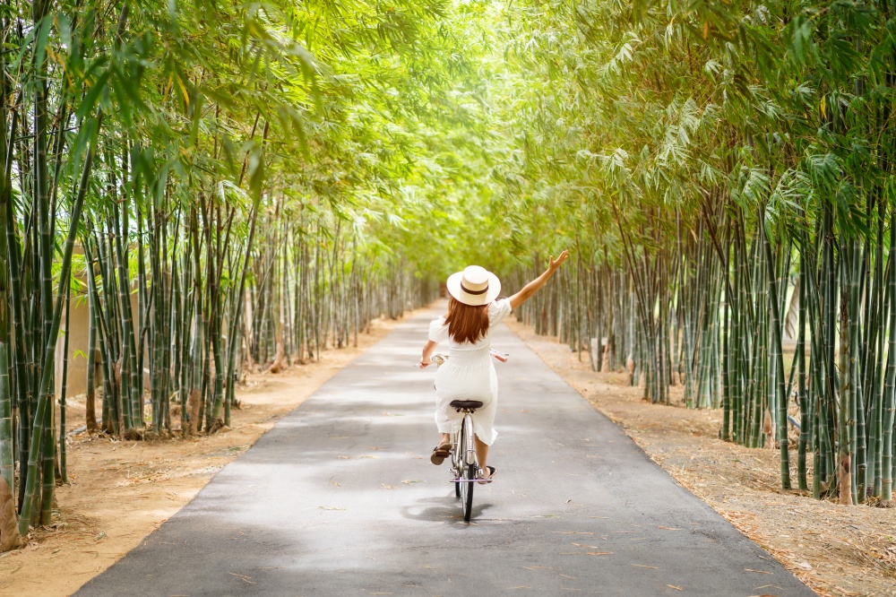 Young happy woman enjoying and riding a bicycle in the bamboo forest while traveling in summer