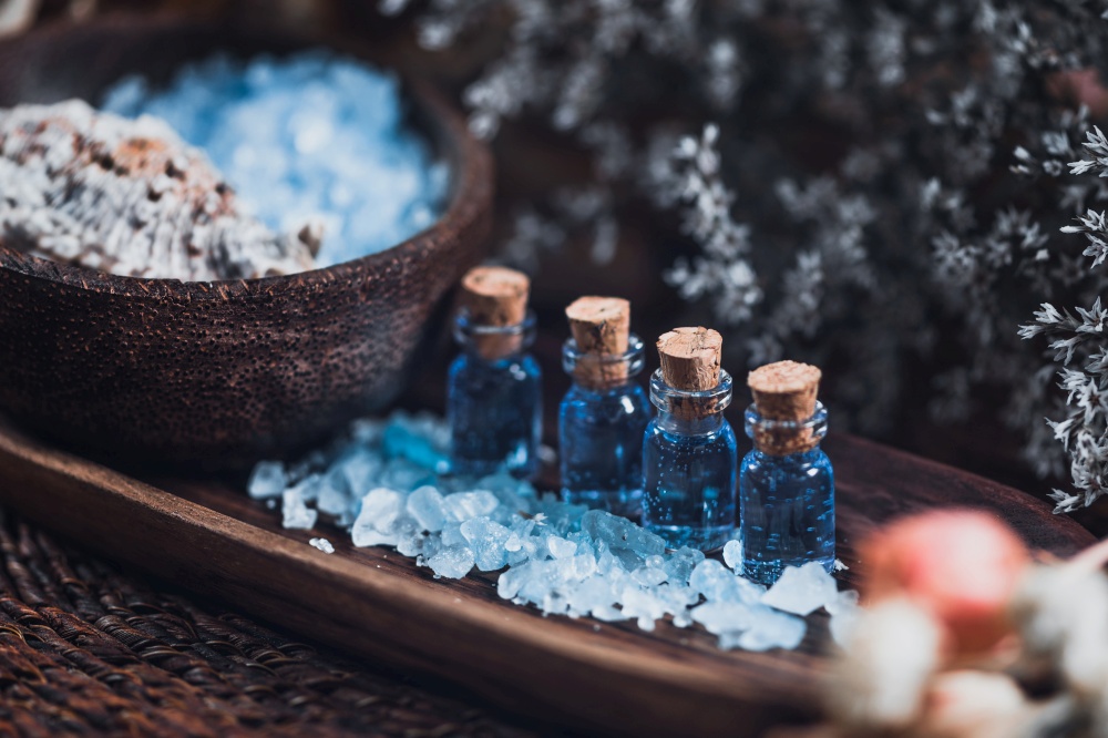 Aromatherapy. Close up photo of wooden and blue spa setting for aromatherapy. Essential oils, sea salt, wooden bowls, white flowers background