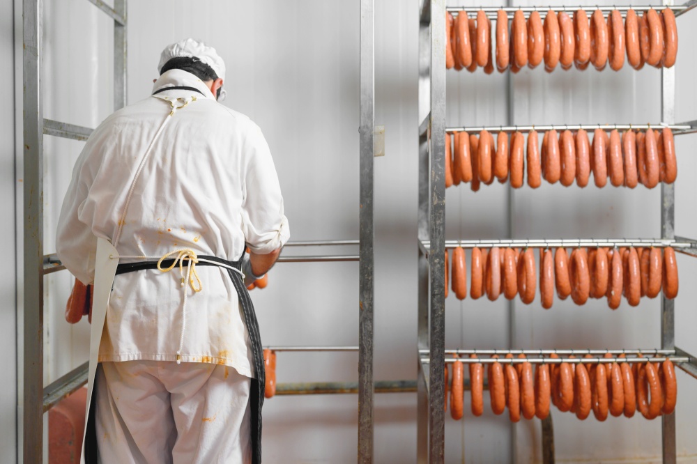 Worker hangs raw sausages on racks in storage room at meat processing factory. High quality photo.. Worker hangs raw sausages on racks in storage room at meat processing factory