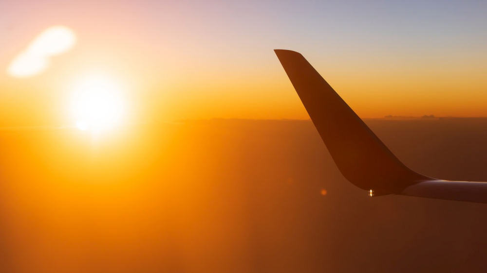 Sunrise view from airplane window seat. Shining sun with lens flare over the wing of plane. Soft focus on the wing.