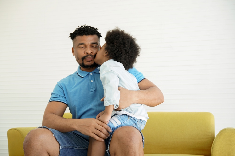 African American family little son kiss his young father at cheek and sitting on sofa at home