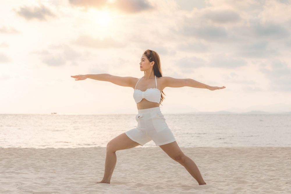 Vacation of Attractive Asian woman relaxing in yoga Warrior one pose on the sand and beach with sunset beautiful sea in Tropical island,Feeling comfortable and relax in holiday,Vacations Concept