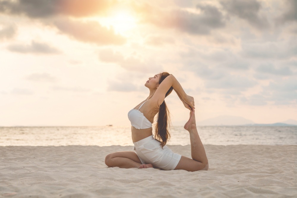 Vacation of Attractive Asian woman relaxing in yoga king pigeon pose on the sand and beach with sunset beautiful sea in Tropical island,Feeling comfortable and relax in holiday,Vacations Concept