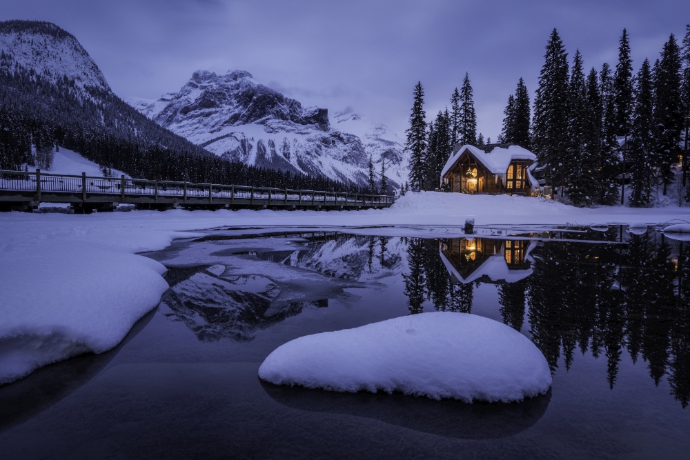 The warm lights of the Emerald Lake Lodge reflect off of the unfrozen portion of Emerald Lake at blue hour within Yoho National Park.