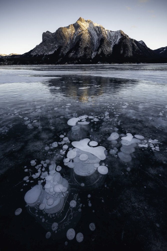 The abstract methane ice bubbles of Abraham Lake as Mount Michener catches the last rays on sunlight in the evening.
