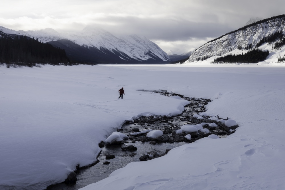 A lone hiker on the snow covered expanse of Spray Lakes within Kananaskis Country of Alberta.