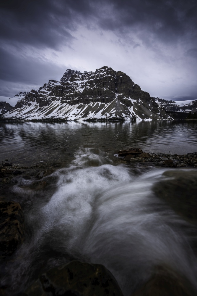 A small stream pours into Bow Lake on a moody morning during early June.