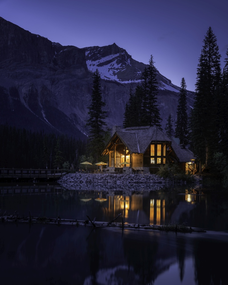 A summer blue hour shot of the warm lights of the Emerald Lake Lodge reflecting in the foreground waters.