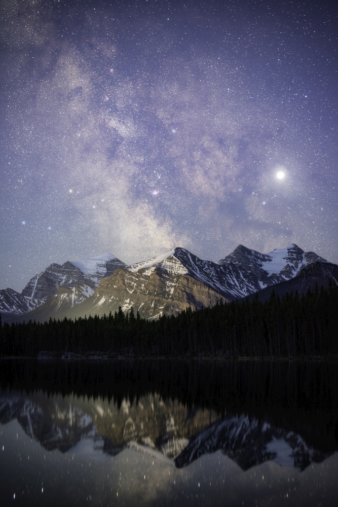 A closeup view of the Milky Way shining high over the Canadian Rockies, reflecting off of the calm waters of Herbert Lake.