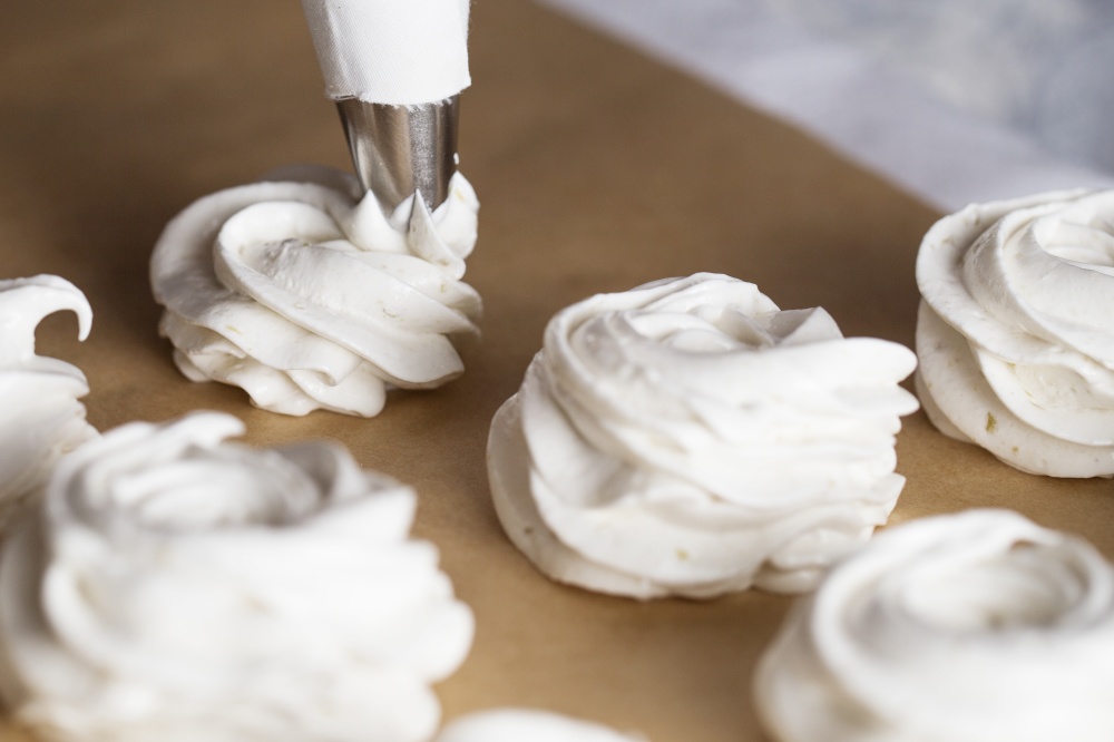 The process of making marshmallow. Close up hands of the chef with confectionery bag cream to parchment paper at pastry shop kitchen