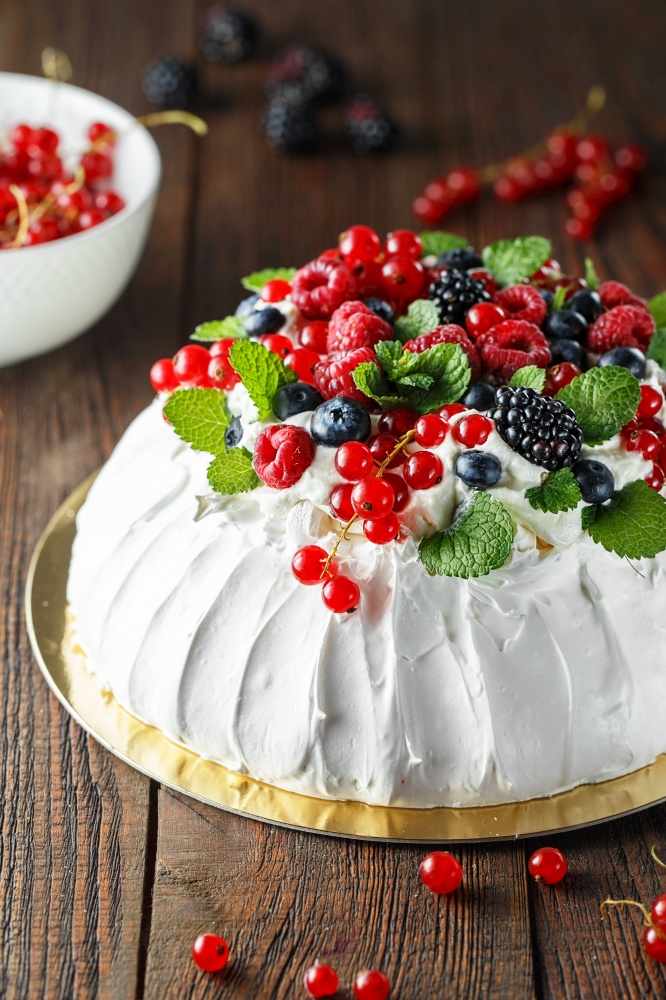 Pavlova cake with cream and fresh summer berries on wooden background. Close up of Pavlova dessert with forest fruit and mint. Food photography