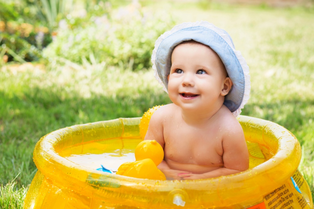 beautiful baby girl in Cotton Panama Cap bathes in Inflatable Swimming Paddling Pool outdoors