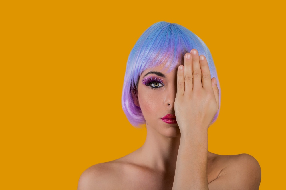 Young sensual woman in short colorful wig having bright makeup covering one eye looking unemotional. . Vivid vogue model covering eye