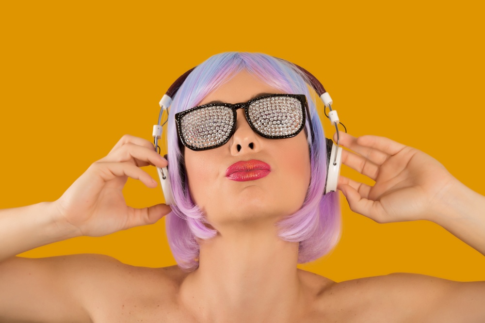 Bright rebellious girl in wig and glam sunglasses listening to music confidently. . Trendy glamorous woman in headphones