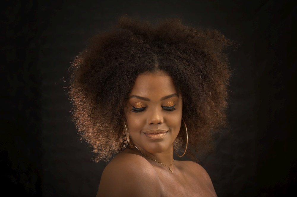Sensual young woman with Afro hairstyle wearing makeup and hoop earrings closing eyes on black background. Gorgeous black model with makeup and hairstyle