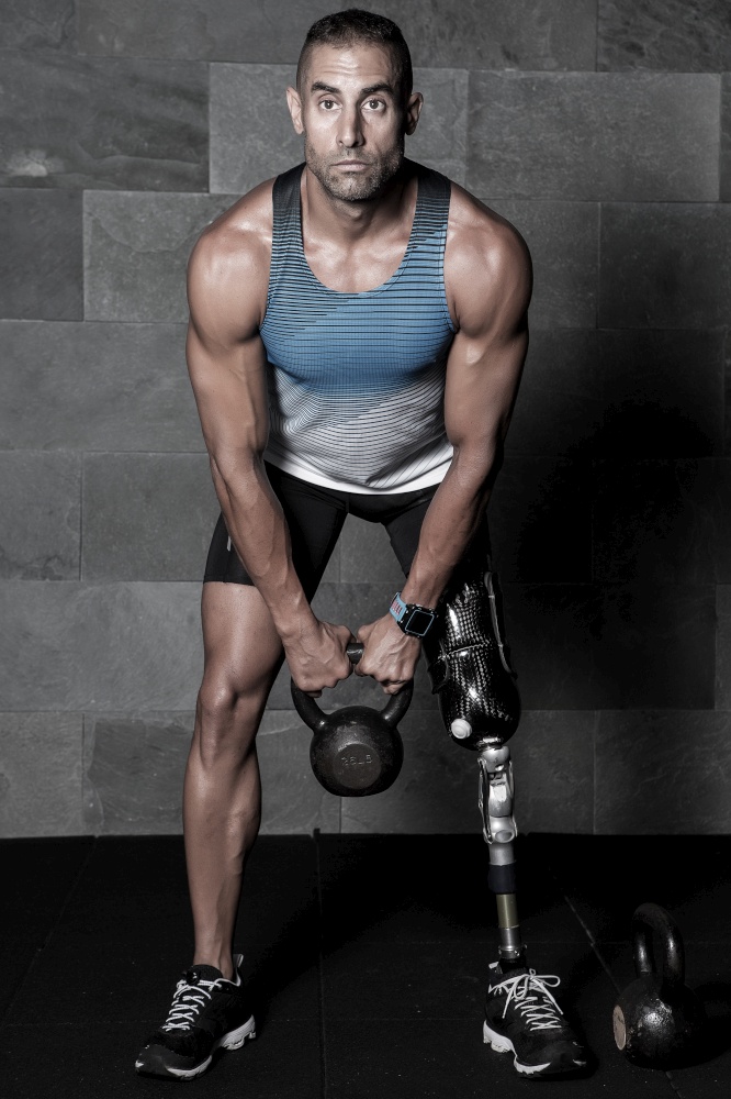 Confident muscular athlete with artificial leg limb doing squats with kettlebell in gym. Sportive man with prosthesis training with kettlebell