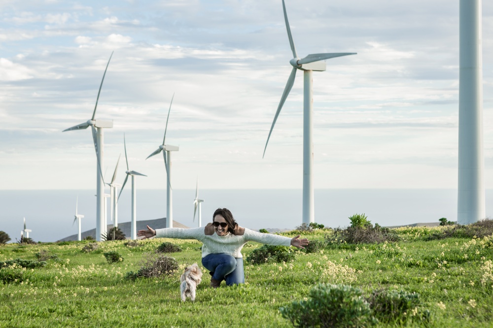 Content female owner playing with cute little dog in field on background of windmills on Lanzarote. Smiling woman playing with dog in meadow with windmills