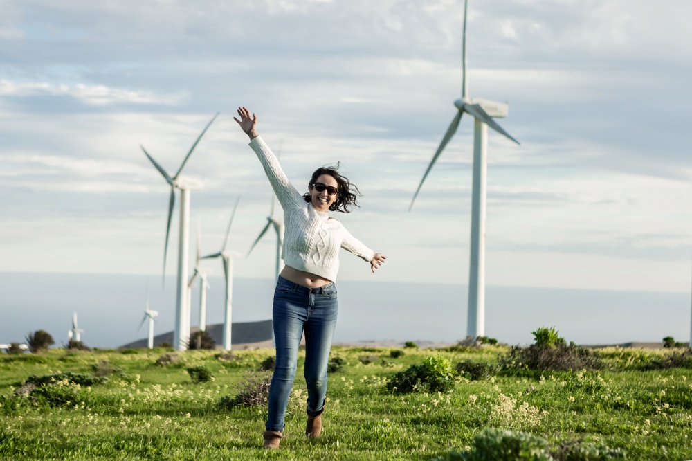 Happy female with outstretched arms enjoying freedom in field with windmills while spending weekend on Lanzarote and looking at camera. Delighted woman with outstretched arms in meadow
