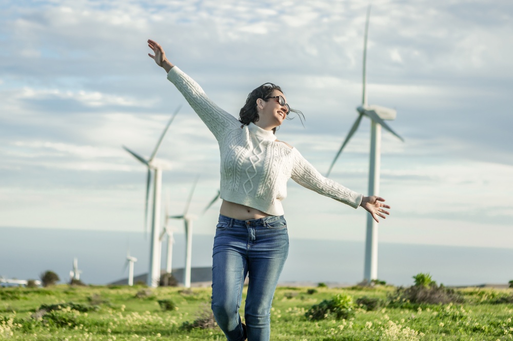 Content female standing with outstretched arms in meadow and enjoying summer weekend on background of windmills on Lanzarote. Carefree woman standing in field with windmills on sunny day
