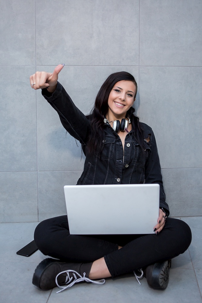 Smiling woman with laptop sitting and gesturing thumb up.. Smiling woman with laptop gesturing