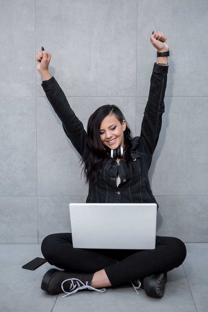 Cheerful woman sitting at laptop and celebrating with hands up.. Woman celebrating at laptop