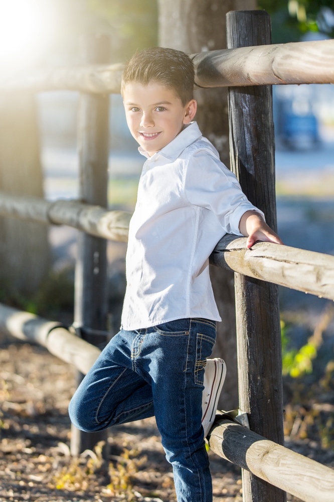 Charming stylish boy posing on rural fence looking confidently at camera.. Dandy kid posing confidently
