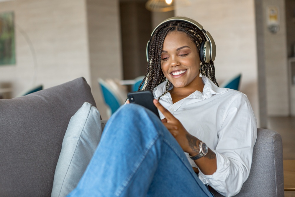 Front view of woman listening to music with headphones and using mobile phone while leaning on a sofa at home. Concept of people in home.. Front view of woman listening to music with headphones and using mobile phone while leaning on a sofa at home