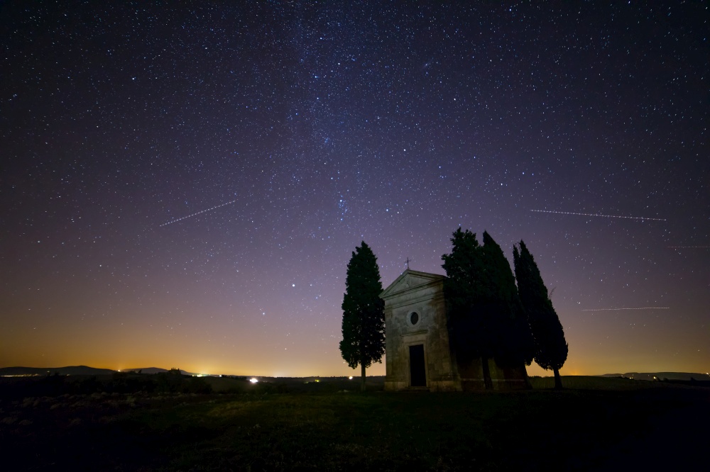 Italy. Tuscany. Lonely chapel and cypress trees in a field. Night sky with myriads of stars. Starry Sky over Church