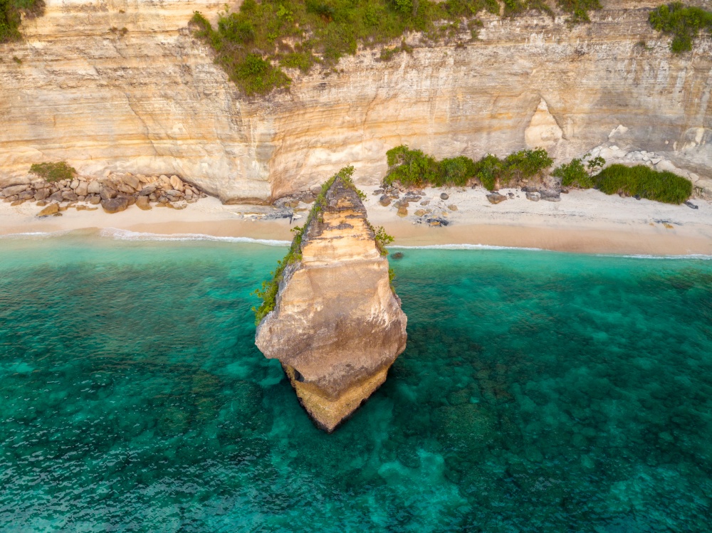 Indonesia. A narrow strip of empty wild beach near the rocky shore. Lonely scenic island near the shore. Aerial view. Wild Tropical Beach and Rock. Aerial View