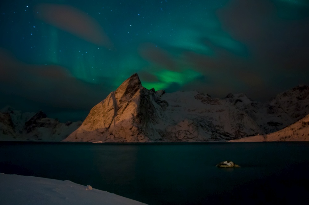Norway at night. Winter fjord surrounded by snow-capped mountains. Northern lights and clouds. Northern Lights and Clouds over the Mountains
