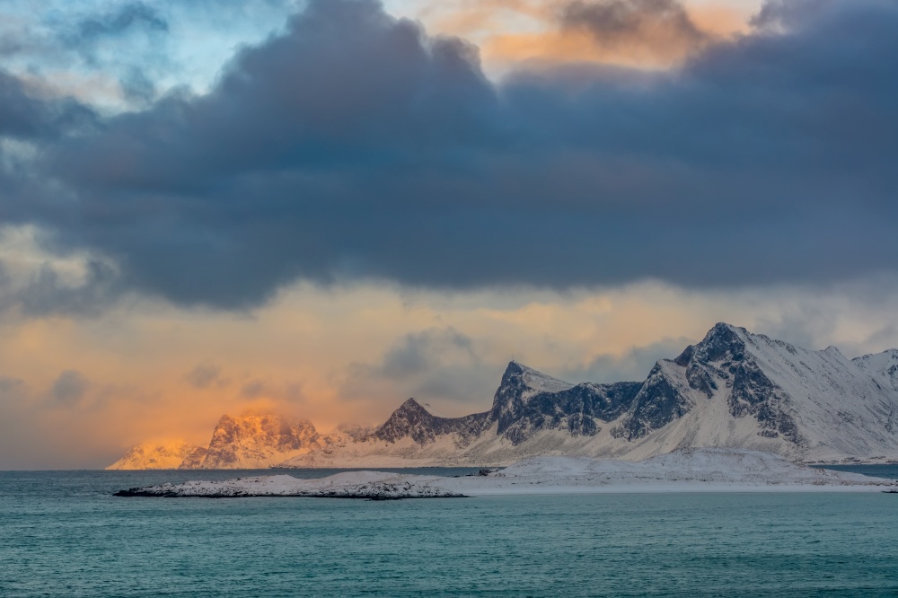 Winter Norway. Deserted mountainous coast of the ocean. Thick clouds and sunlight. Clouds and Sunlight over the Winter Norwegian Gulf