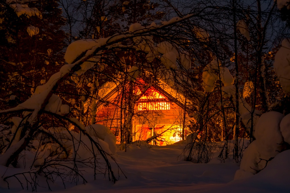 Northern Finland. Thick winter forest and a lot of snow. Small wooden house and night lighting. Lighted Wooden House in the Night Winter Forest