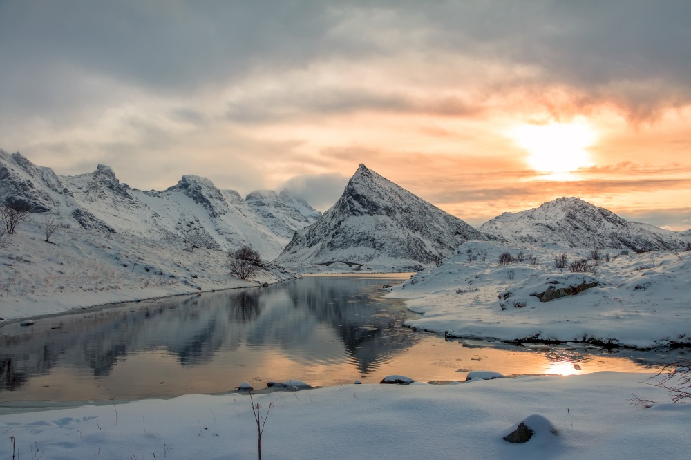 Small bay of the Norwegian fjord surrounded by snow-capped mountains. Winter evening. Norwegian Fjord among Winter Mountains at Sunset