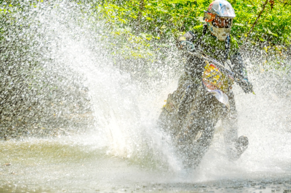 Summer enduro. Sunny weather. The athlete overcomes the stream with a large number of splashes. Sport Bike Driver and Water Spray