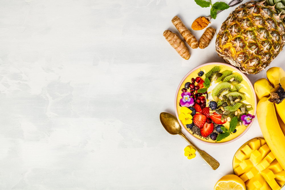 Mango banana pineapple turmeric breakfast superfoods smoothie bowl topped with fruits, berries and seeds. Overhead top view flat lay
