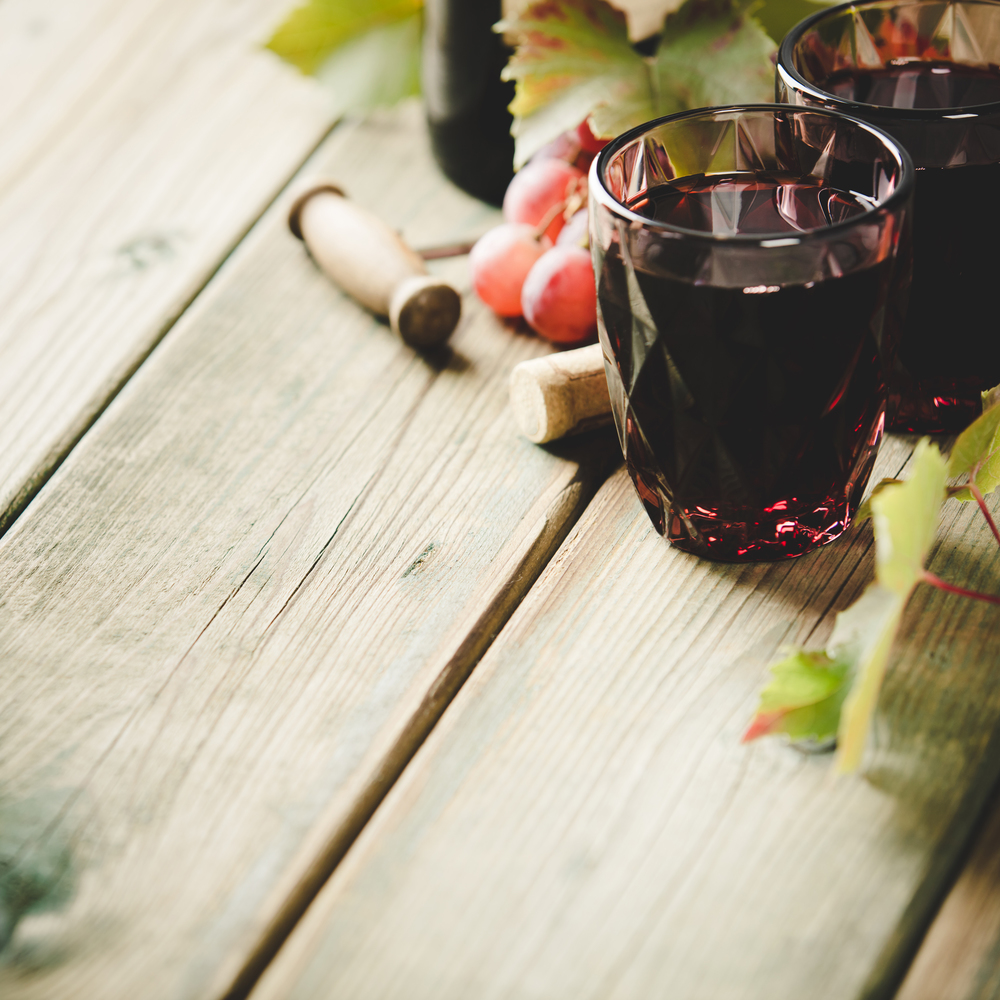Red wine composition. Red wine glasses, bottle of wine, grapes and leaves on rustic background. Space for text
