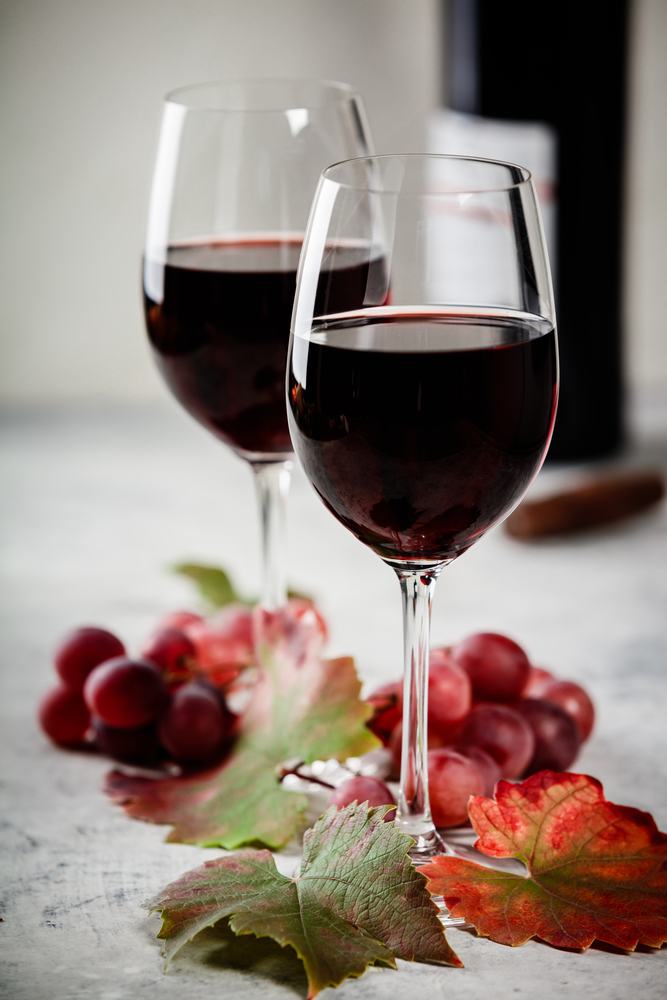 Red wine composition. Red wine glasses, bottle of wine, grapes and leaves on rustic background. Space for text