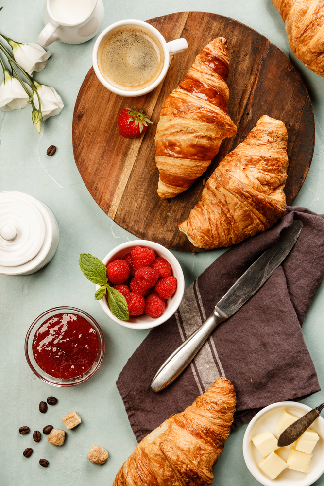 Continental breakfast captured from above top view, flat lay . Coffee, orange juice, croissants, jam, berry, milk and flowers. Blue concrete worktop as background. Layout with free text copy space.. Continental breakfast captured from above on concrete background