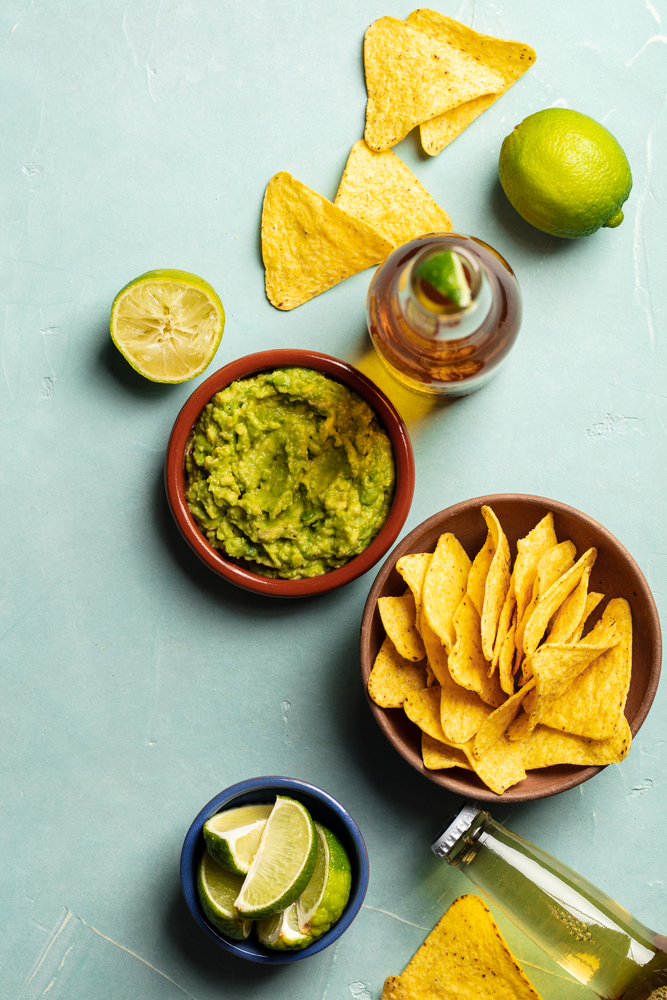 Nachos, guacamole and beer on blue background, flat lay