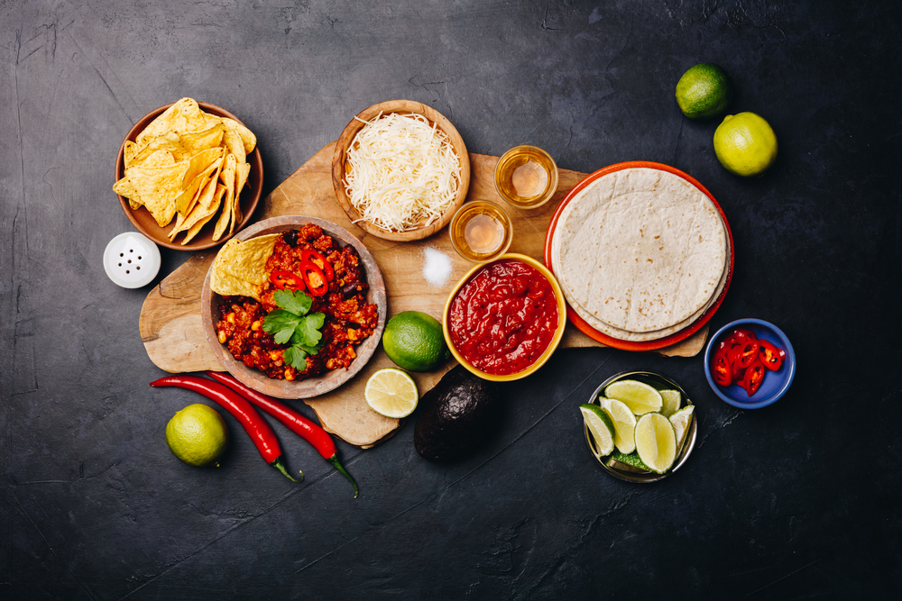 Concept of Mexican food corn tortillas, nachos, salsa, avocado, limes, cheese, chili con carne flat lay. Concept of Mexican food, flat lay, dark background